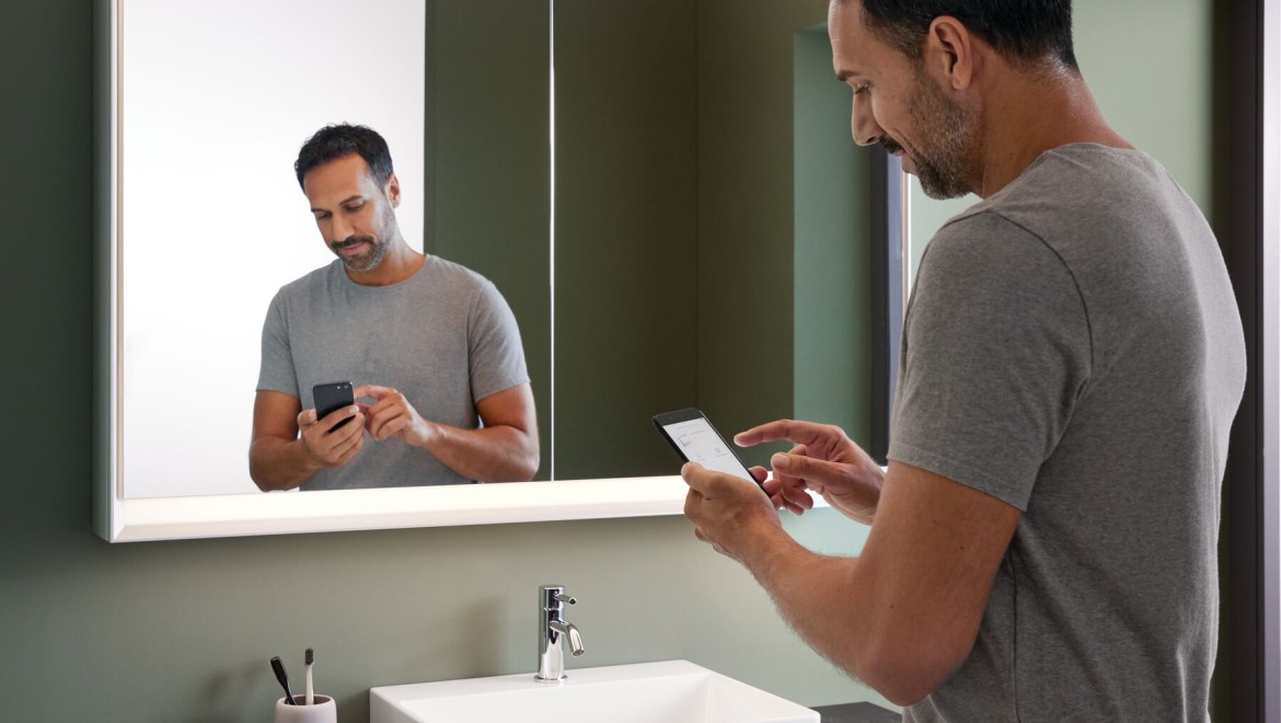 Muž stojící v koupelně s mobilním telefonem