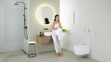 Žena opírající se o umyvadlo v koupelně se sprchovací toaletou Geberit AquaClean Sela a koupelnovým nábytkem a umyvadlem Geberit VariForm