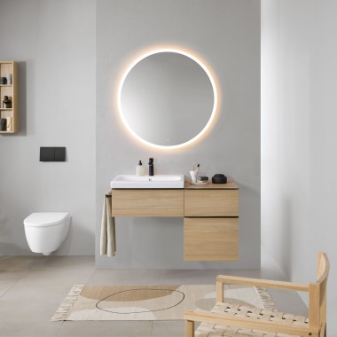 Koupelna s šedými stěnami, dřevěným koupelnovým nábytkem Geberit a kulatým zrcadlem Geberit Option s osvětlením