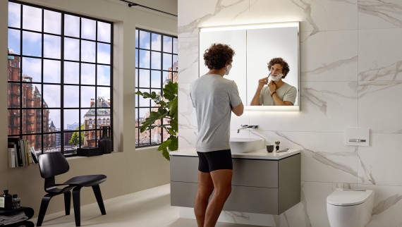 Muž holící se u umyvadla s koupelnovým nábytkem a zrcadlovou skříňkou Geberit ONE