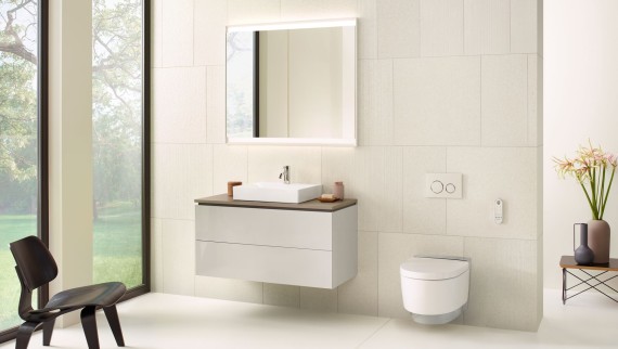 Bílá koupelna se zrcadlovou skříňkou, umyvadlovou skříňkou, ovládacím tlačítkem a keramickými prvky od společnosti Geberit