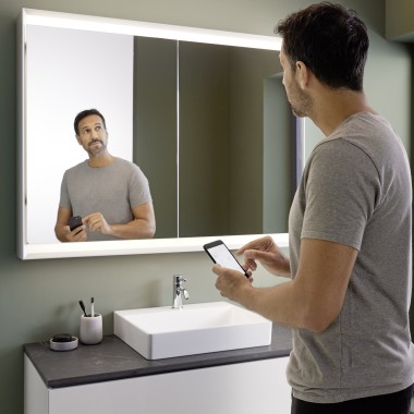 Man controls lighting of the Geberit ONE mirror cabinet with his smartphone (© Geberit)
